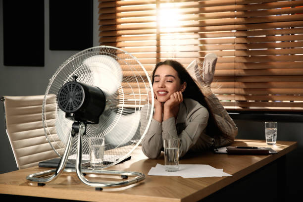 istock Woman enjoying air flow from fan while lying on table at workplace. Summer heat 1358835259