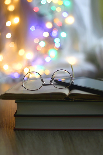 Stack of books, digital e-reader and reading glasses. Colorful bokeh lights in the background. Selective focus.