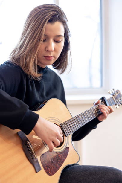 poważna młoda kobieta grająca na gitarze akustycznej w domu. - 20s acoustic guitar adult art zdjęcia i obrazy z banku zdjęć