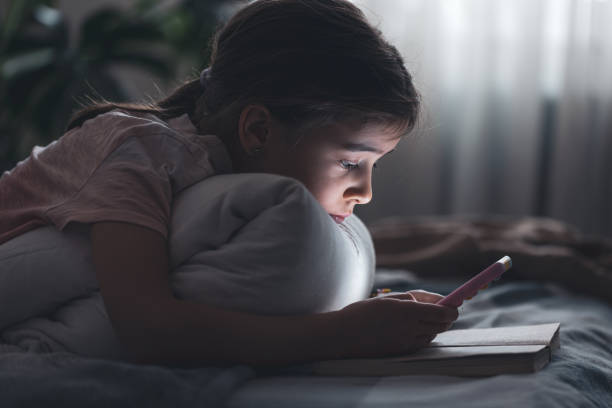 a little girl uses the phone, holding a book in her hands. - sleeping child bedtime little girls imagens e fotografias de stock