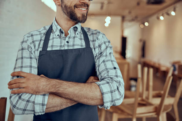 istock Joyful bearded man in apron keeping arms crossed 1358842817