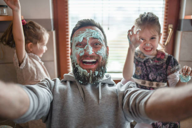 istock Bearded Male Playing With Child Daughters While Cooking Dessert And Getting Face Dirty With Topping 1358843360