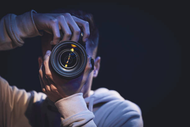 un fotografo uomo con una macchina fotografica scatta una foto al buio, nello spazio di copia. - conceptual symbol flash foto e immagini stock