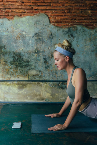 istock Young Woman Using Mobile Phone for Yoga Tutorial at Home 1358843427