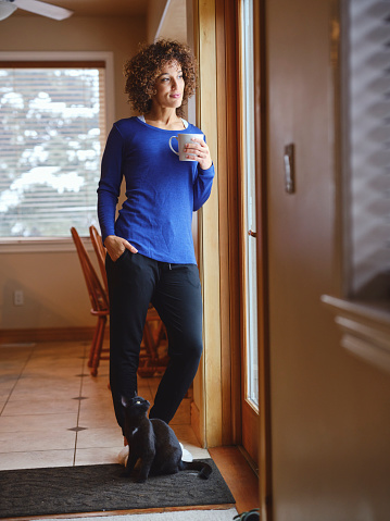 A woman in her home, standing by a window looking out at the winter scene.