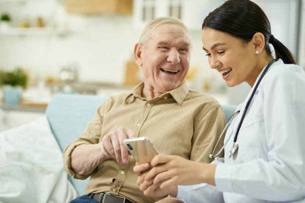 istock Happy nurse and senior citizen sitting on sofa and using mobile phone 1358844755