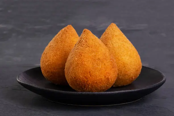 traditional fried coxinha on a black plate on a slate background - brazilian snack.