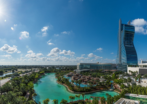 A young attractive girl looks down on the hotel complex on the first coastal line of the sea. Beautiful green area with pool and places for relaxation. The concept of tourism, vacations, and recreation.