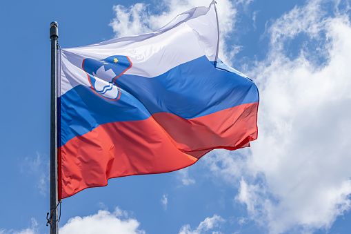 Slovenian national flag waving on blue sky background. Republic of Slovenia, SL