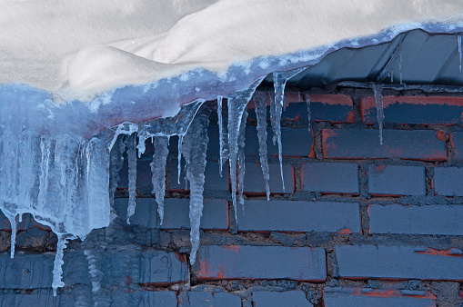 Icicles and snow drifts on the old roof against the background of the old painted brick wall
