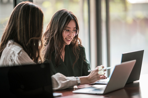 Two Asian ladies having a discussion in the office with laptops