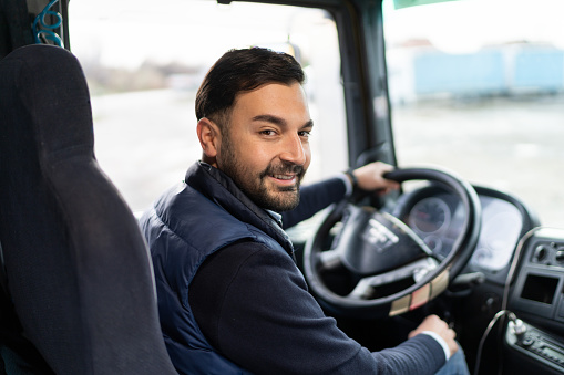 Smiling truck driver sitting in cabin, and looking at camera