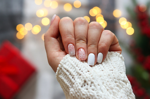 Idea of the winter manicure. Woman's hand with gel polish manicure white color and with snowflakes ornament against festive Christmas background. Selective focus.