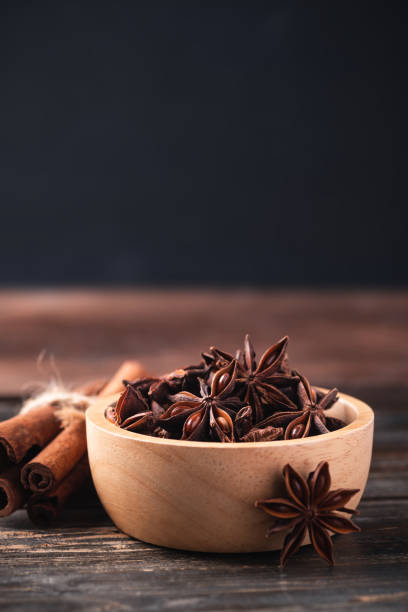 Star anise in bowl and cinnamon stick on wooden background