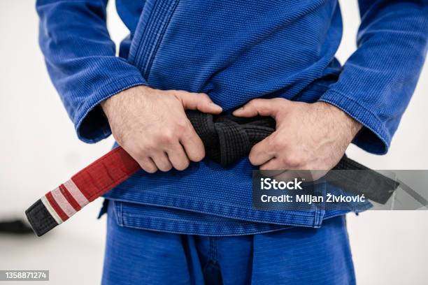 Close Up On Midsection Of Unknown Caucasian Male Athlete Bjj Brazilian Jiujitsu Black Belt Standing On The Mat At Academy Holding His Belt During Training Wearing Blue Gi Front View Stock Photo - Download Image Now