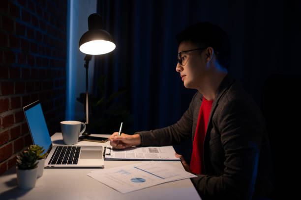 istock Portrait of Serious asian young man using computer and typing in dark room. 1358878546