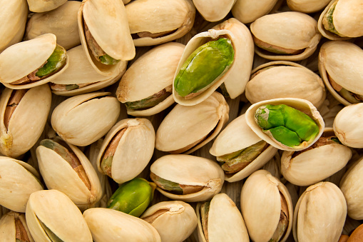 Stock photo showing close-up view of shelled pistachio nuts piled high in a green dish against a green background. Raw pistachios are considered to be a very healthy snack food and are high in vitamin B6, potassium, antioxidants and protein, boasting a list of health benefits and may aid weight loss.