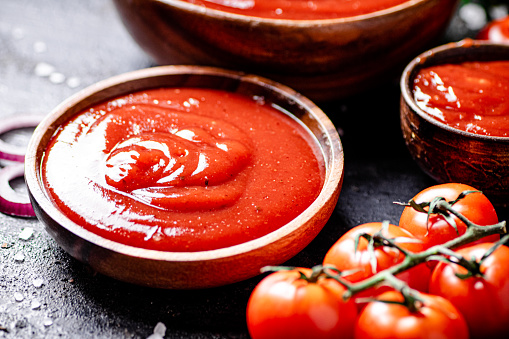 Tomato sauce in a wooden plate. On a black background. High quality photo