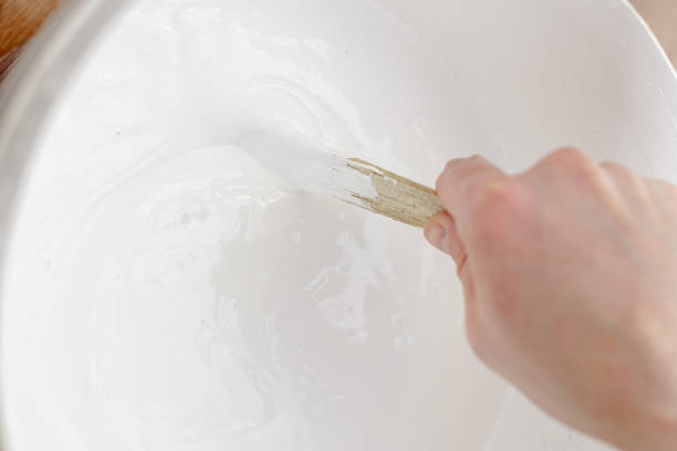 화가의 손은 나무 막대기와 항아리에 흰색 페인트를 혼합합니다. 홈 수리. - paint mixing stick 뉴스 사진 이미지