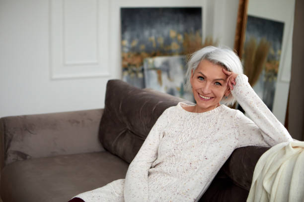 Stylish woman with gray hair on couch stock photo