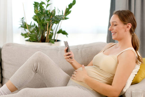 istock Pregnant woman watching media content on mobile phone while sitting on sofa 1358895332