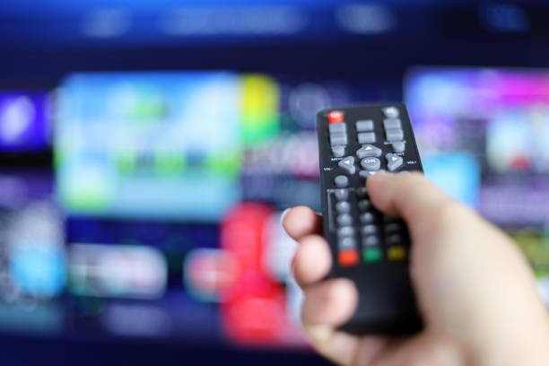 Remote controller in female hand on smart TV screen background stock photo