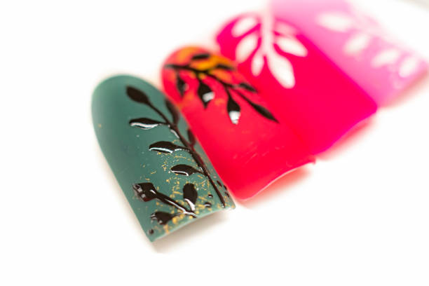 Green matte nail tip closeup. Autumnal gel polish color, black floral painting, small pieces of golden foil. Selective focus on the details, object isolated on white background.