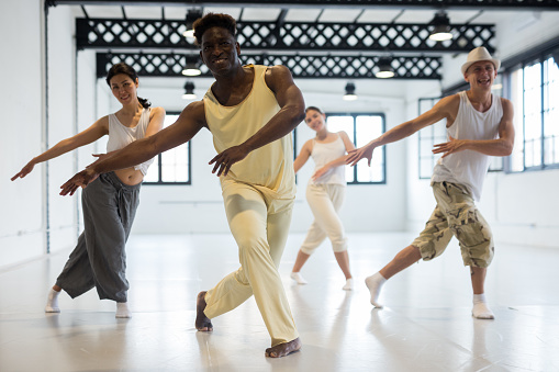 Positive afro american man studying movement of contemporary dance in classroom with his friends
