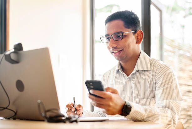 istock Smiling young businessman working from home using a laptop and smart phone 1358905161