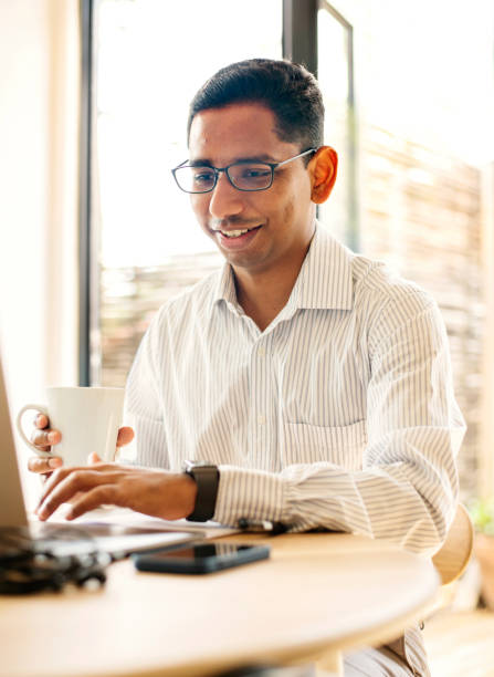 Smiling young businessman drinking coffee and working on a laptop at home stock photo