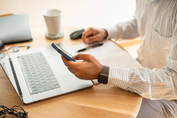 istock Businessman checking his phone while working on a laptop at a table 1358905203