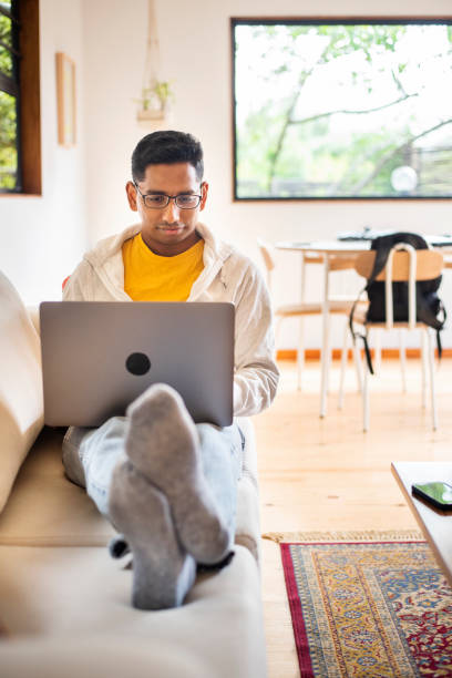 istock Young man lying on his sofa and working on a laptop 1358905356
