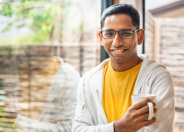 istock Smiling young man drinking coffee by a window at home 1358905469