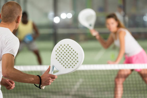 jugador de pádel jugando al pádel en una pista de pádel interior detrás de la red - deporte de raqueta fotografías e imágenes de stock