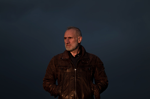 Portrait of adult man in brown leather jacket against blue sky during sunset