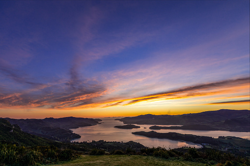 This October 2021 dawn, composite, long-exposure image shows Te Whakaraupō Lyttelton Harbour in Aotearoa New Zealand. The area is part of Horomaka Banks Peninsula in the city of Ōtautahi Christchurch. Te Moana-nui-a-Kiwa Pacific Ocean can be seen in the distance. Multiple exposures are stacked to improve the quality of the dark landmass.