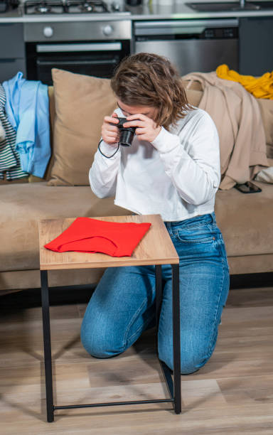 vue d’une jeune femme qui tire un t-shirt rouge sur une table. elle est dans le marketing en ligne. elle va le vendre. elle gagne de l’argent en vendant ses affaires d’occasion. - photographer women retro revival camera photos et images de collection