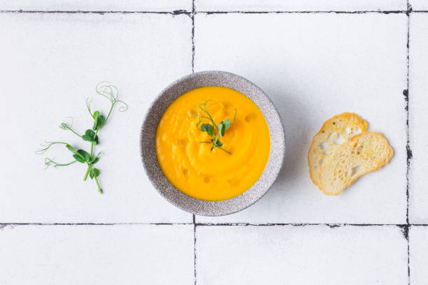 Pumpkin and carrot cream soup on white tile background with croutons. Top view stock photo