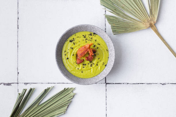 istock Green soup puree with grilled bacon on tile background palm leaves 1358909938