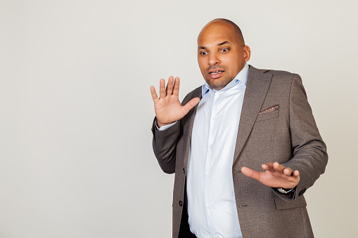 Portrait of shocked young African American businessman guy, scared and frightened by fear expression, stopped hand gesture, shouting in shock. Panic concept. Standing on a gray background