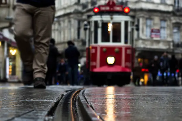 People walking down Istiklal street on a rainy day and red tram