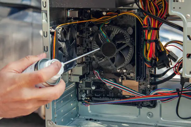 Photo of Maintenance and cleaning of the insides of the computer. Man's hand holds a cylinder of compressed air and cleans the insides of the computer