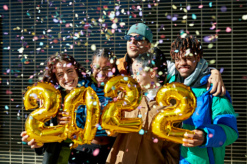 Portrait of five diverse friends celebrating the New Year's together in the street with confetti.