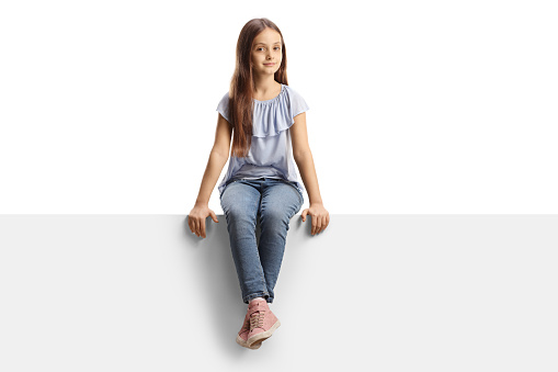 Girl sitting on a blank panel and looking at camera isolated on white background