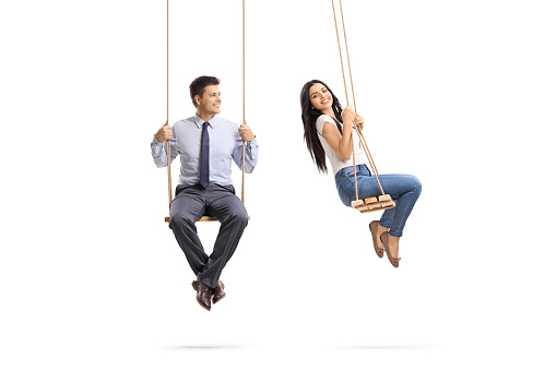 Man sitting on a swing and looking at a beautiful young woman swinging isolated on white background