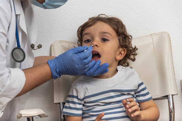 Doctor taking a swab for corona virus sample from potentially infected caucasian boy mouth.Covid-19 laboratory test.Medical staff with PPE suit test coronavirus covid-19. stock photo
