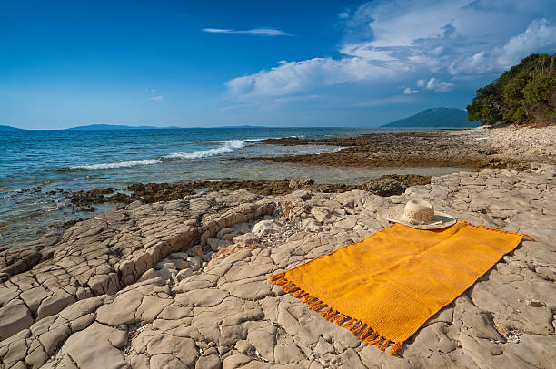 Wild Adriatic sea beach with orange rug. Croatia, Losinj island. stock photo