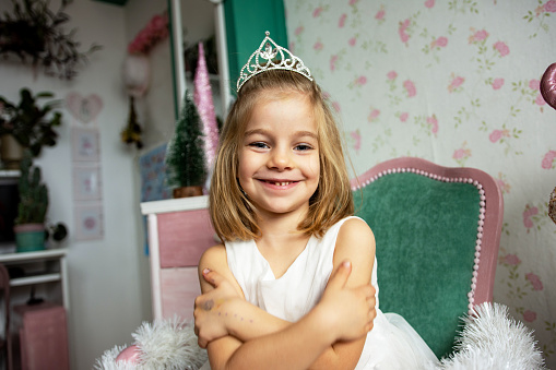 Cute little girl wearing tiara, sitting and smiling at Christmas time