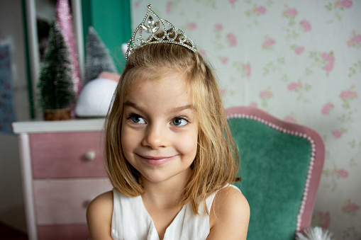 Cute little girl wearing tiara, sitting and smiling at Christmas time