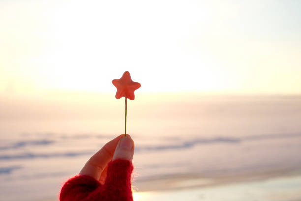 istock Hand holding red christmas star on winter snow and sky background with copy space 1358928036